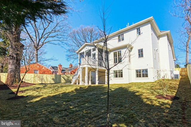 rear view of house featuring a lawn, fence, and a sunroom