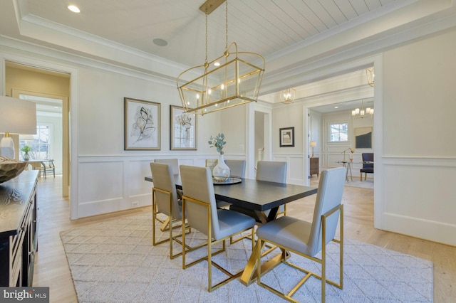 dining space with light wood finished floors, wainscoting, a raised ceiling, and crown molding