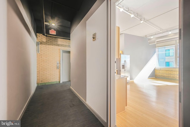 hall with rail lighting, brick wall, baseboards, and wood finished floors