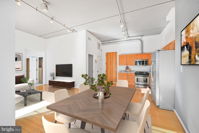 dining space featuring visible vents, a high ceiling, rail lighting, and light wood-style floors