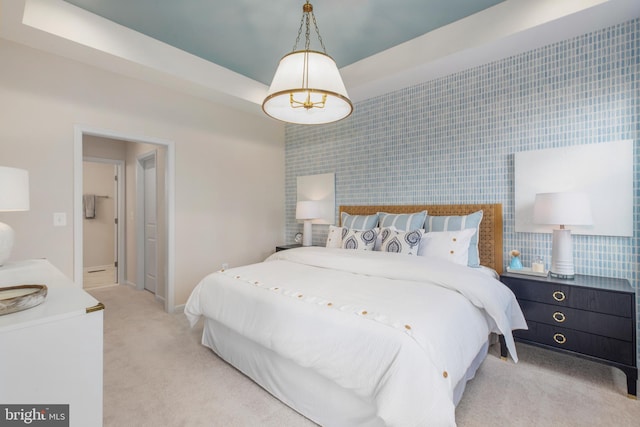 bedroom featuring light carpet, an accent wall, baseboards, and a raised ceiling