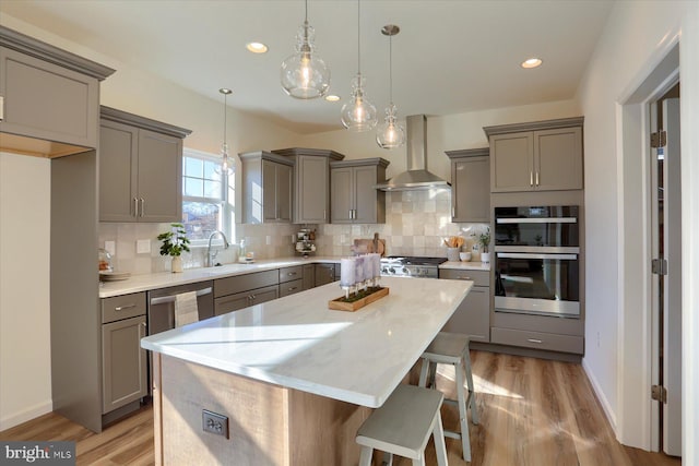 kitchen featuring stainless steel appliances, hanging light fixtures, gray cabinetry, a kitchen island, and wall chimney range hood