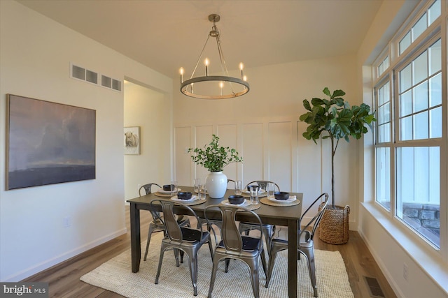 dining room with dark wood finished floors, visible vents, a decorative wall, and a notable chandelier