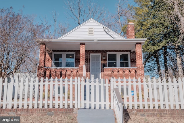 bungalow-style house with a fenced front yard, a chimney, a porch, and brick siding