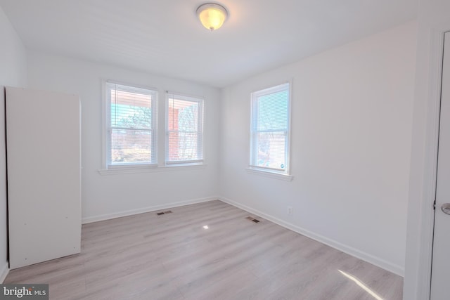 empty room featuring light wood-style flooring, visible vents, and baseboards