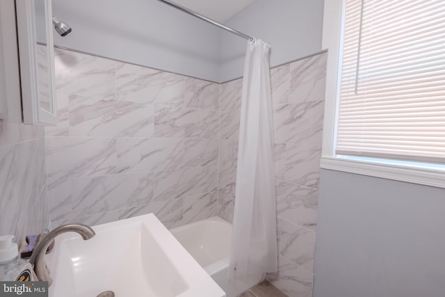 bathroom featuring a healthy amount of sunlight, shower / bath combo, tile walls, and a sink