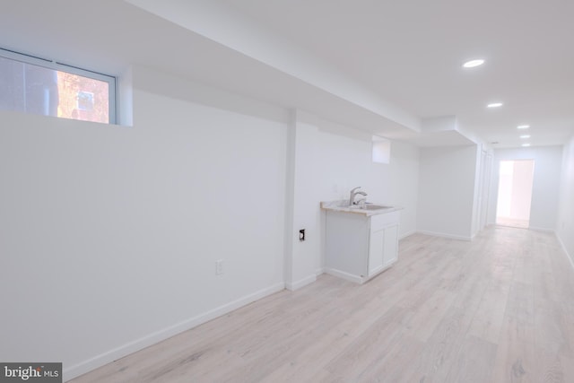 below grade area featuring recessed lighting, light wood-type flooring, a sink, and baseboards