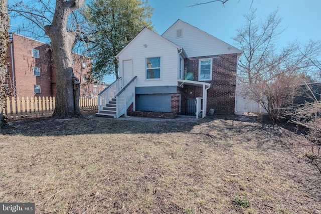 view of front of home featuring brick siding, a front lawn, fence, and stairway