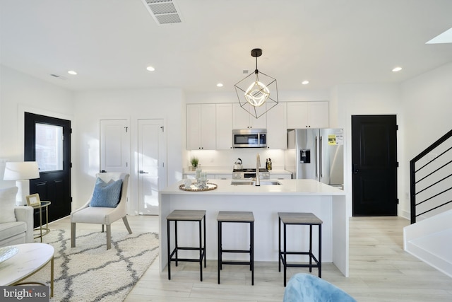 kitchen with decorative light fixtures, stainless steel appliances, light countertops, white cabinets, and a sink