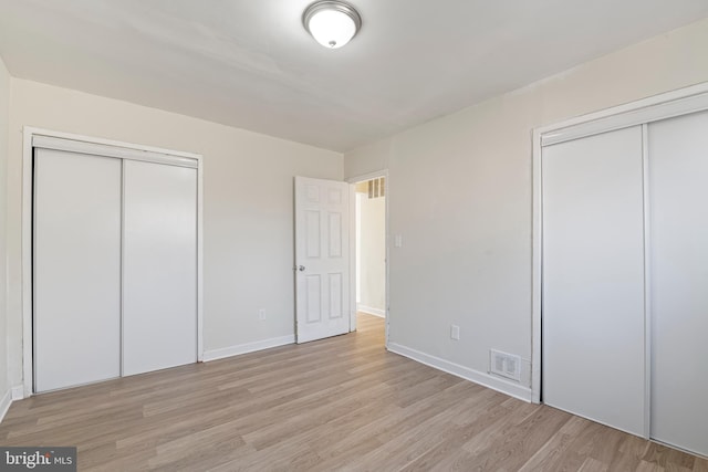 unfurnished bedroom featuring light wood-type flooring, baseboards, visible vents, and two closets