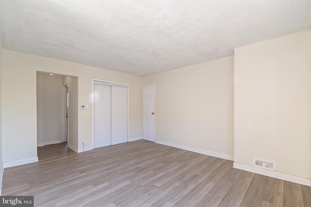 unfurnished room featuring light wood-style floors, baseboards, and a textured ceiling