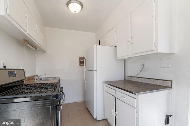 kitchen with stainless steel gas range oven, light tile patterned flooring, a sink, white cabinetry, and freestanding refrigerator