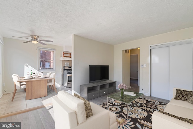 living area featuring light wood-style flooring, visible vents, ceiling fan, and a textured ceiling