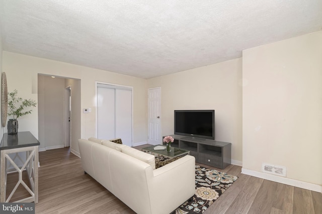 living room with a textured ceiling, baseboards, and wood finished floors