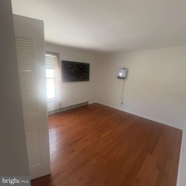 spare room with wood finished floors, baseboards, and a baseboard radiator