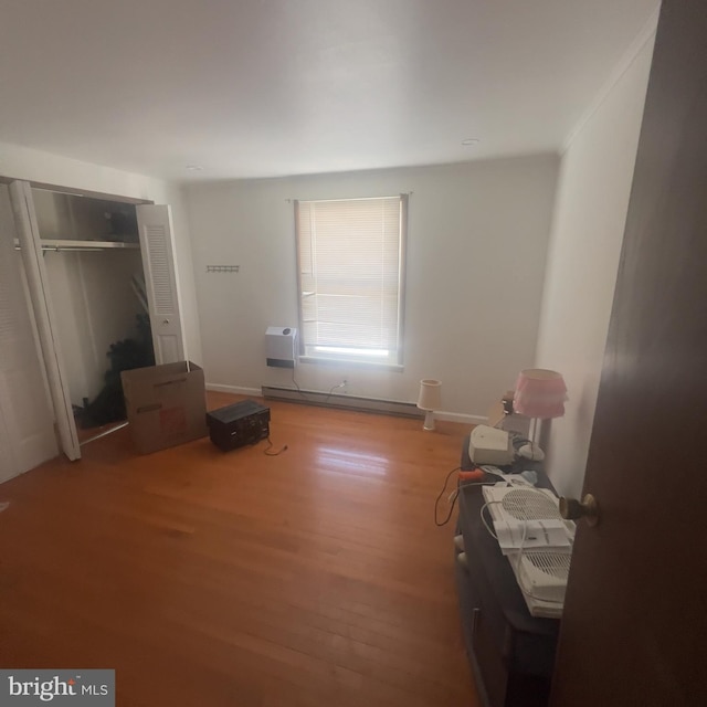 bedroom with wood finished floors, a closet, baseboard heating, and baseboards