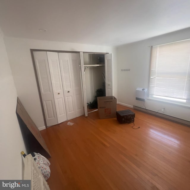 unfurnished bedroom featuring a closet, wood finished floors, a baseboard heating unit, and a wall mounted AC