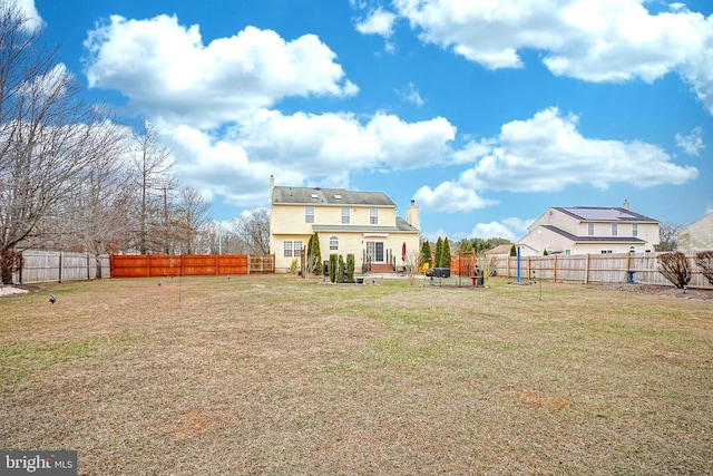 rear view of house featuring a fenced backyard, a chimney, and a lawn