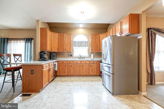 kitchen with a peninsula, a sink, baseboards, light countertops, and appliances with stainless steel finishes