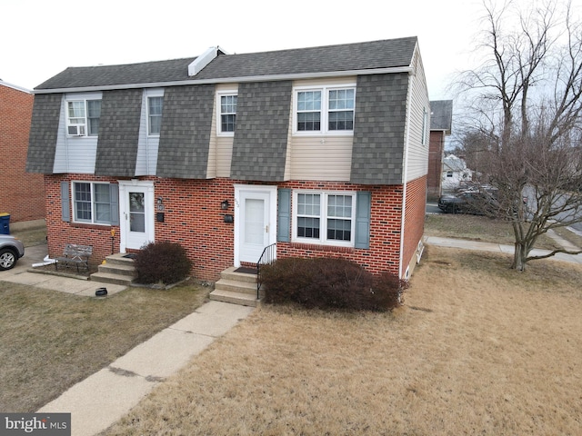 view of front of house featuring entry steps, brick siding, roof with shingles, and a front yard