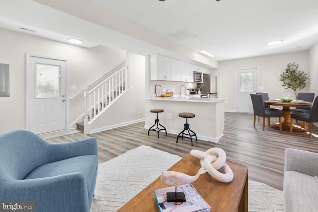 living room featuring electric panel, baseboards, stairway, and light wood finished floors