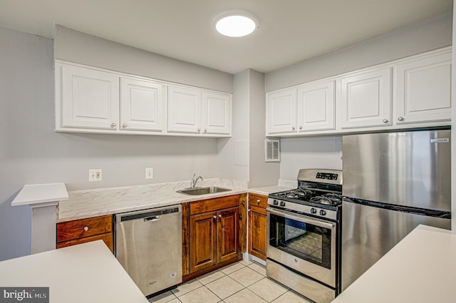 kitchen with light tile patterned floors, stainless steel appliances, a sink, white cabinets, and light countertops