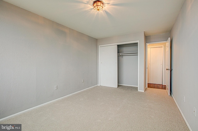 unfurnished bedroom with a closet, light colored carpet, and baseboards