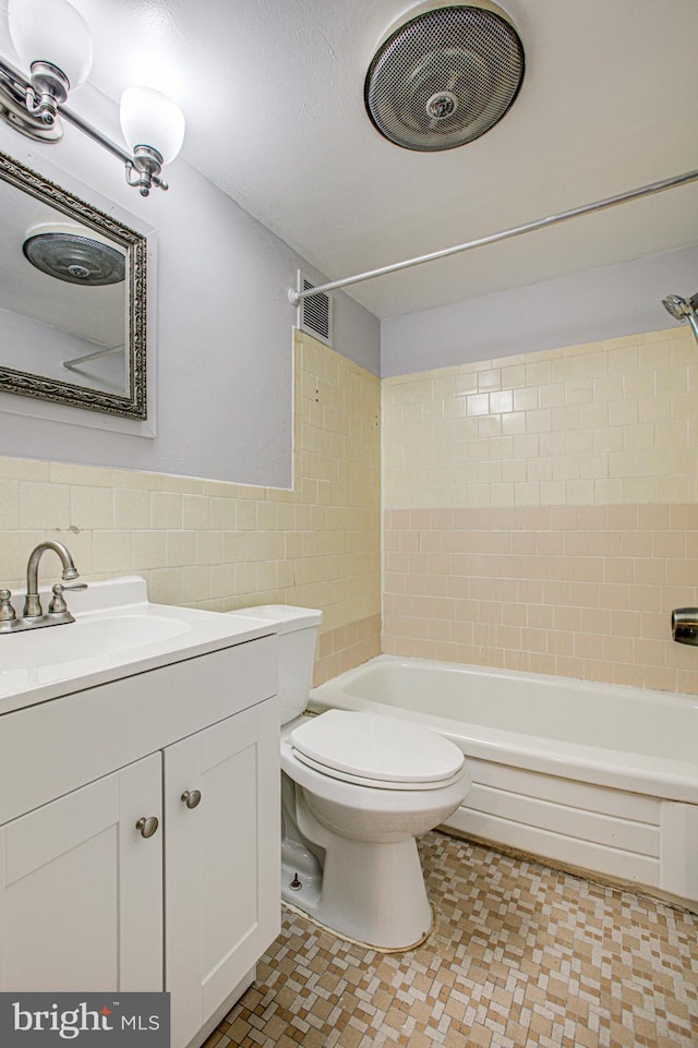 bathroom with a textured ceiling, toilet, vanity, tile walls, and wainscoting