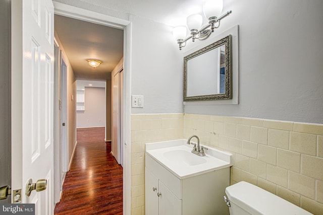 half bathroom with toilet, a wainscoted wall, wood finished floors, vanity, and tile walls