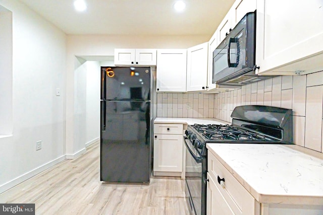 kitchen with tasteful backsplash, light stone counters, light wood-type flooring, black appliances, and white cabinetry