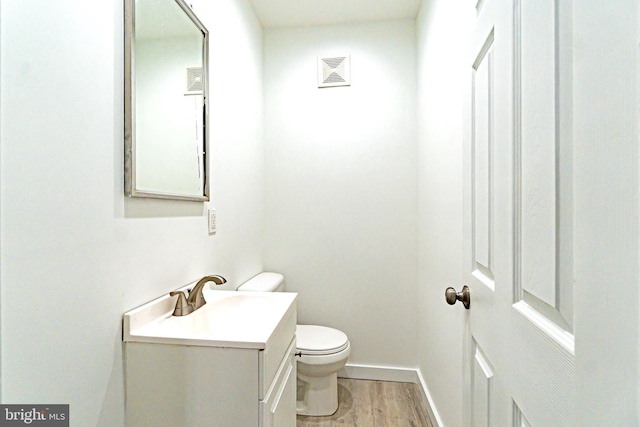 half bath with baseboards, visible vents, toilet, wood finished floors, and vanity