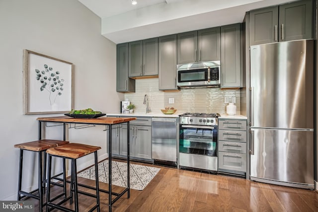 kitchen featuring stainless steel appliances, a sink, light countertops, light wood finished floors, and tasteful backsplash