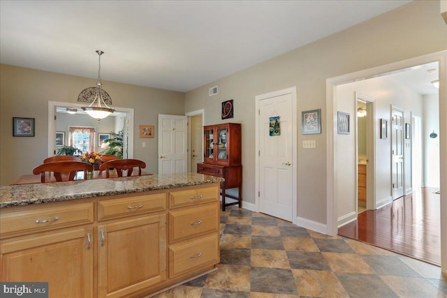 kitchen with light stone counters, visible vents, baseboards, stone finish floor, and pendant lighting