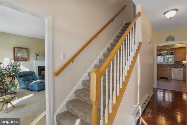 staircase featuring visible vents, baseboards, hardwood / wood-style flooring, a baseboard radiator, and a fireplace