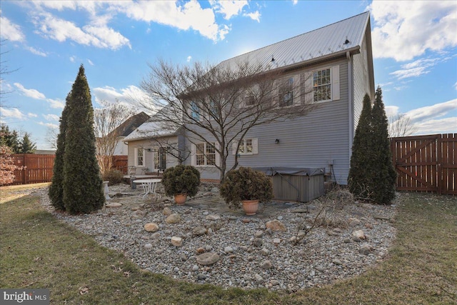 rear view of house with metal roof, a lawn, a fenced backyard, and a hot tub