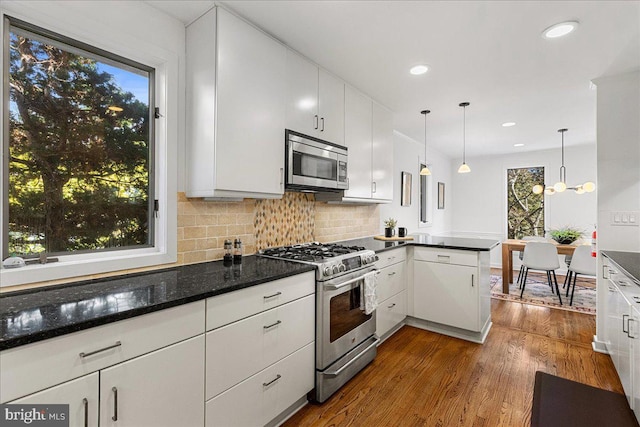 kitchen with stainless steel appliances, a peninsula, dark wood-style flooring, white cabinets, and tasteful backsplash