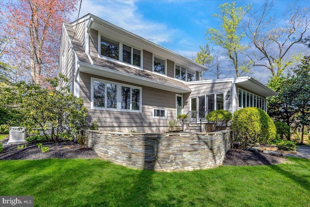 back of house featuring a sunroom, a shingled roof, and a lawn