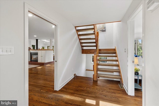 stairs with a glass covered fireplace, visible vents, baseboards, and wood finished floors