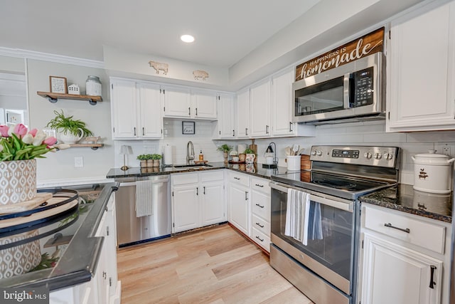 kitchen with light wood finished floors, stainless steel appliances, white cabinetry, a sink, and dark stone counters