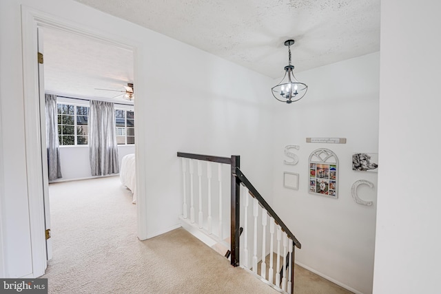 corridor with carpet, a textured ceiling, an upstairs landing, and an inviting chandelier