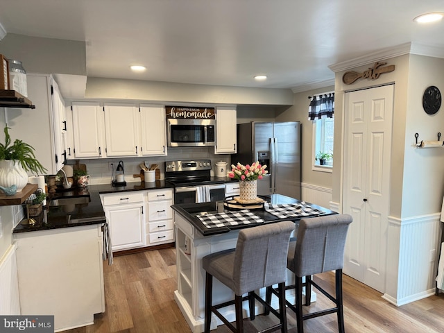 kitchen with a wainscoted wall, a sink, white cabinets, appliances with stainless steel finishes, and dark countertops