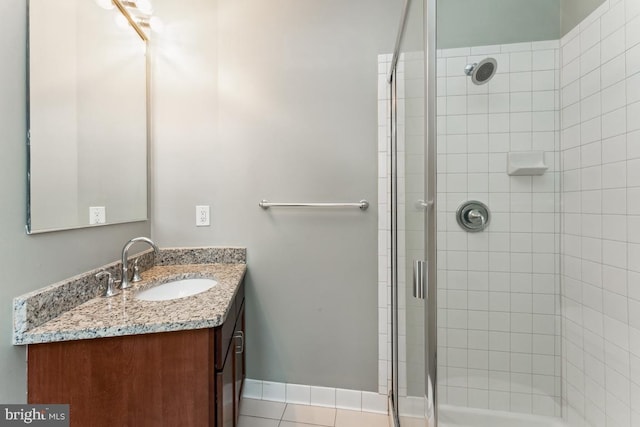 full bathroom featuring tile patterned flooring, a tile shower, vanity, and baseboards