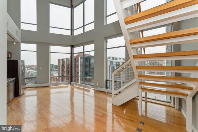 unfurnished living room featuring light wood-style floors, stairway, a towering ceiling, and a city view