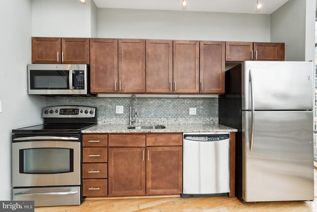 kitchen featuring stainless steel appliances, tasteful backsplash, a sink, and light stone countertops