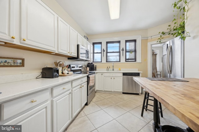 kitchen with appliances with stainless steel finishes, white cabinetry, a sink, and light tile patterned floors