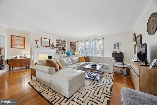 living area featuring light wood-type flooring, built in shelves, a fireplace, and crown molding