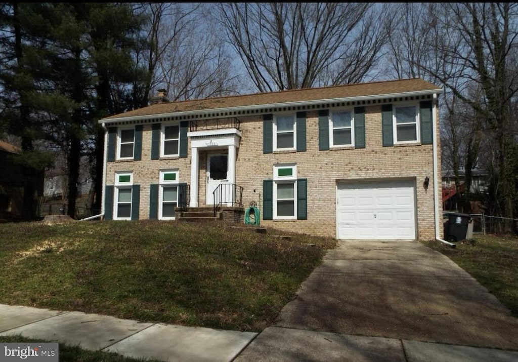 split foyer home featuring an attached garage, brick siding, concrete driveway, a front lawn, and a chimney