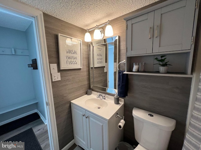 bathroom with wooden walls, baseboards, toilet, a textured ceiling, and vanity