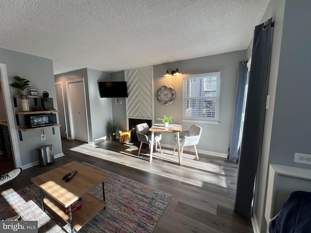 living room featuring a large fireplace, dark wood-style flooring, a textured ceiling, and baseboards