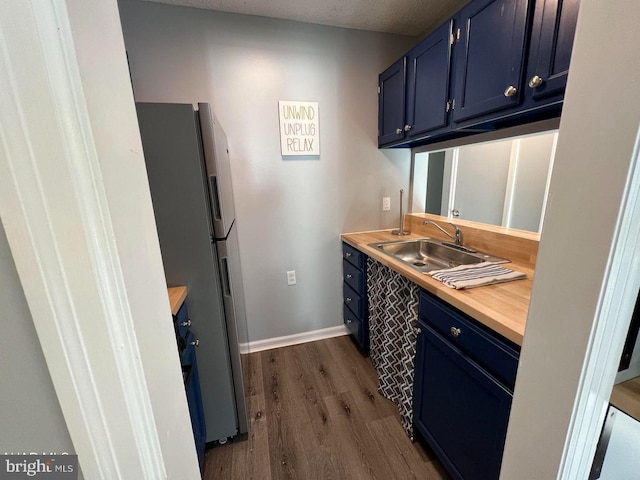 kitchen with dark wood-style flooring, freestanding refrigerator, light countertops, blue cabinetry, and a sink